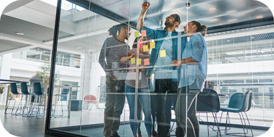 Three team members working together on a glass whiteboard wall